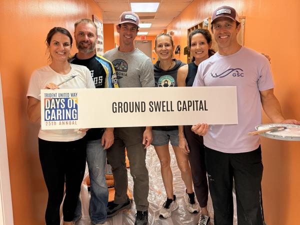 Ground Swell Capital volunteering for a painting project at 2025 Days of Caring. They are posing holding a sign with their name with painting tools