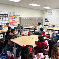 A volunteer reads to a classroom. The students sit quiet as the volunteer is sharing the illustrations from the book