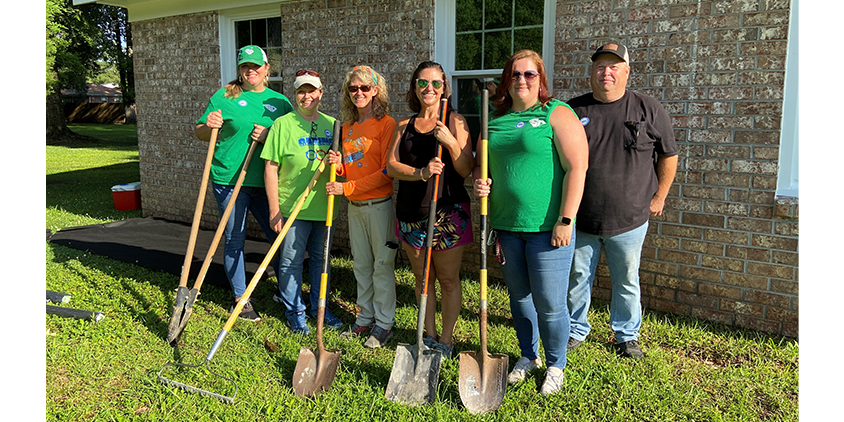 Six volunteers pose for a photo outside holding landscaping tools