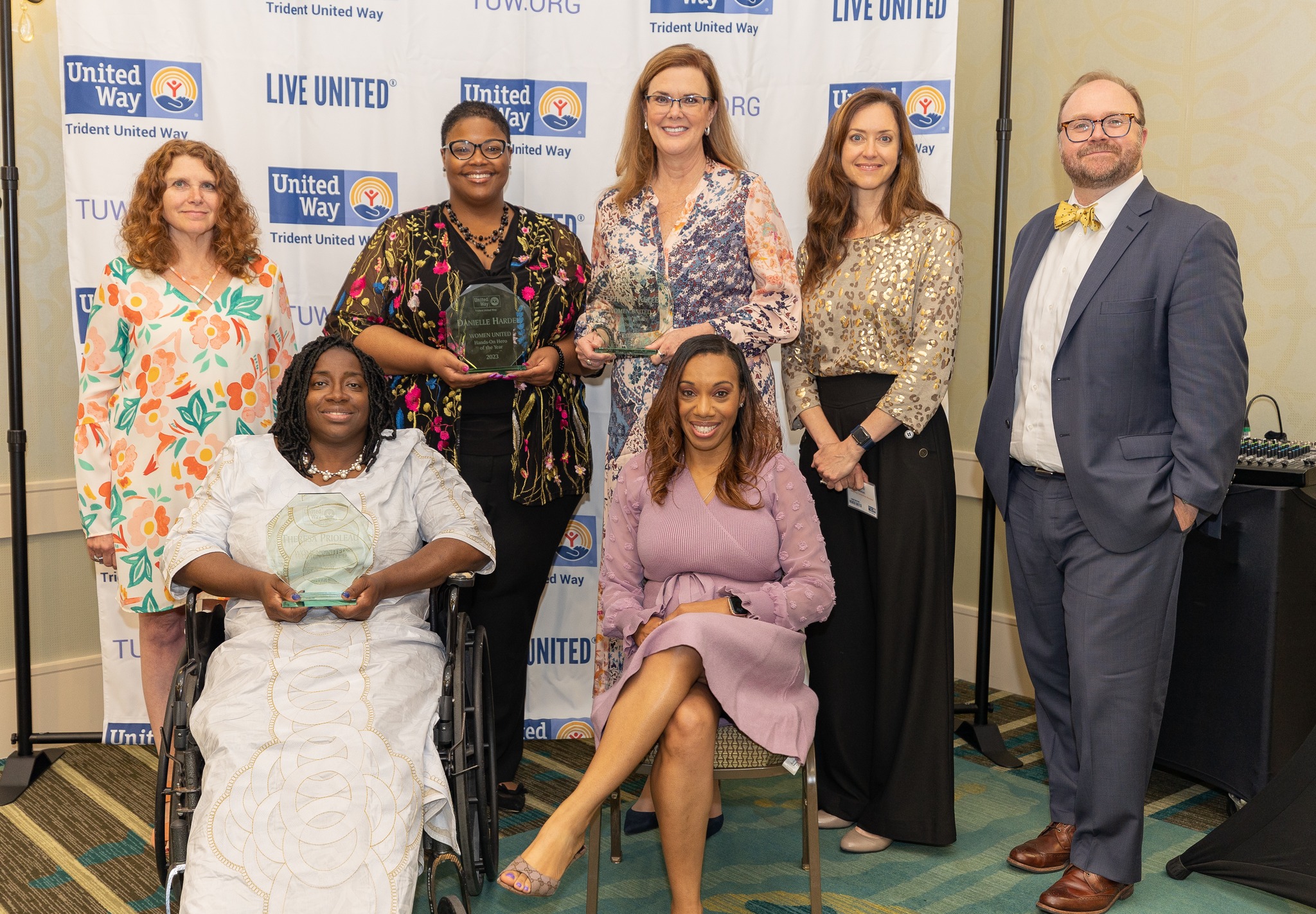 "A group of people including three award nominees smile in front of a Trident United Way background."