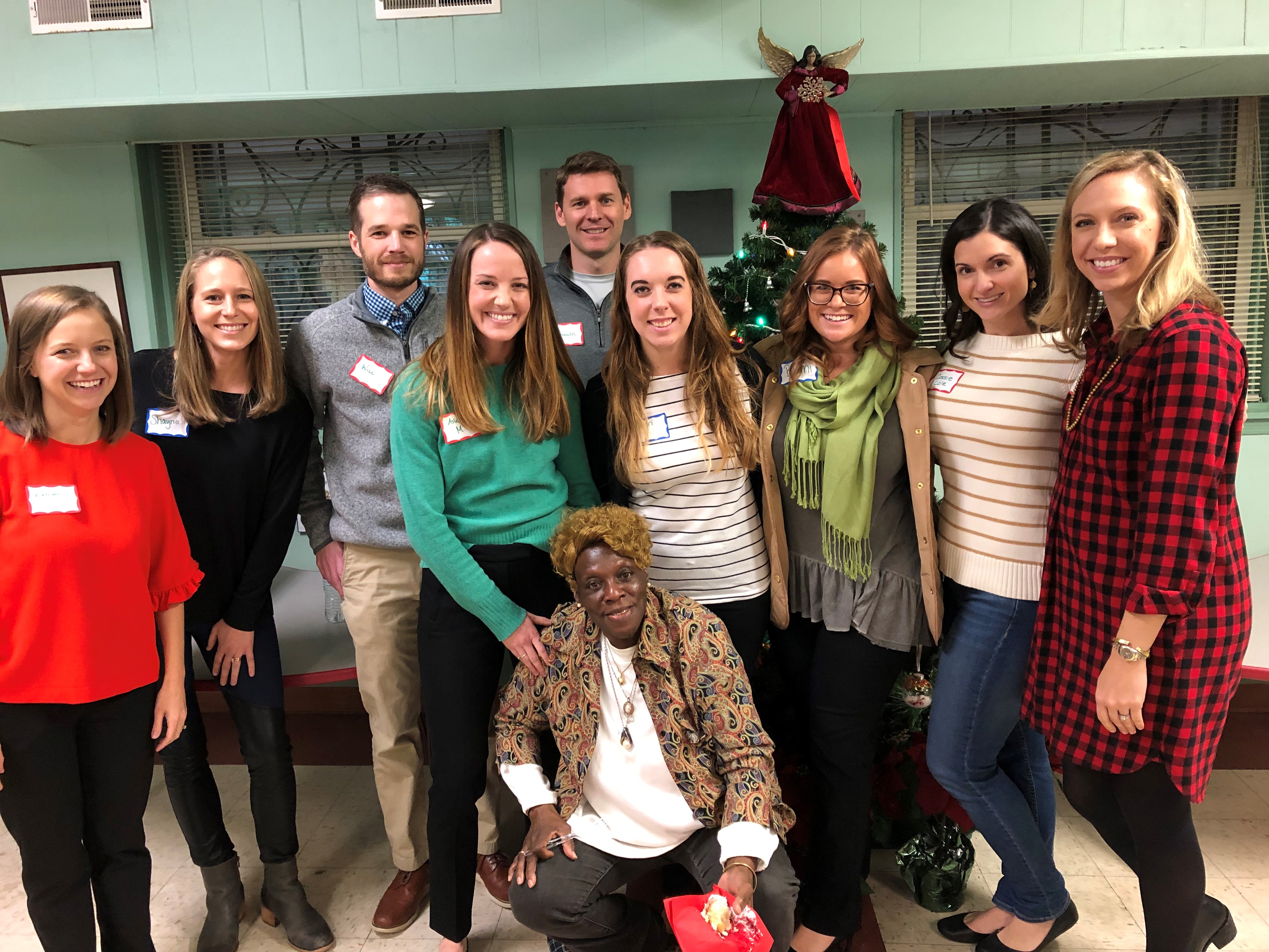 "A group of volunteers stands in front of a Christmas tree with a red festive angel on the top."