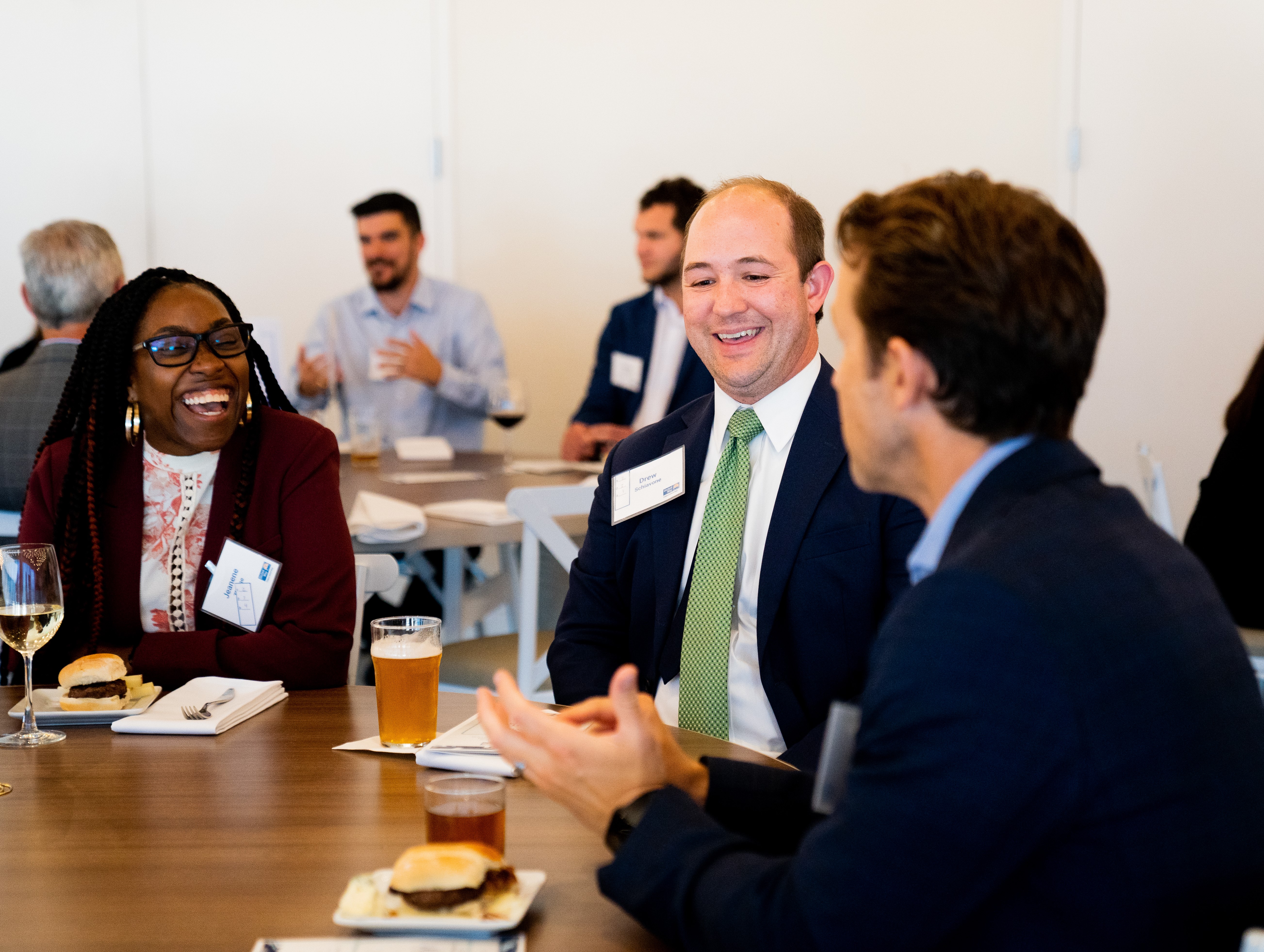 "Three people laugh while discussing around a table. Similar groups can be seen at other tables in the background."