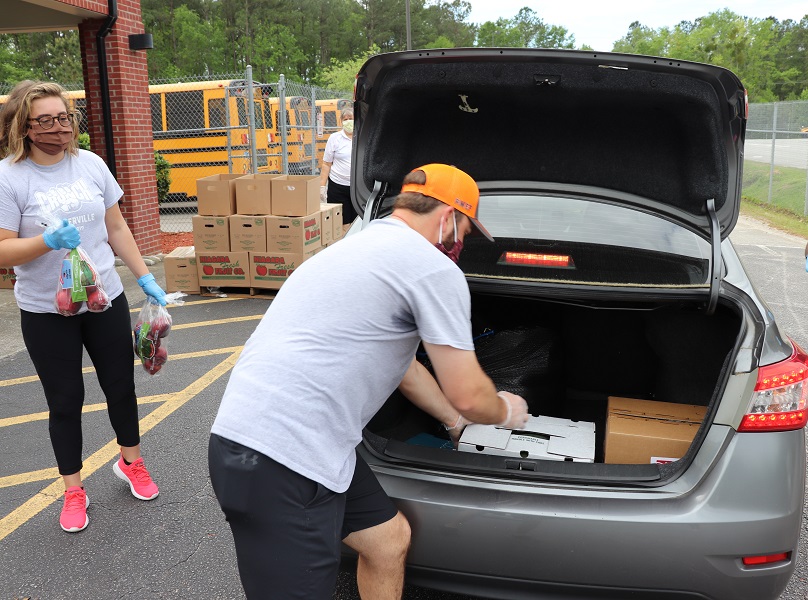 two volunteers helping load the produce into the trunk of someone's car 