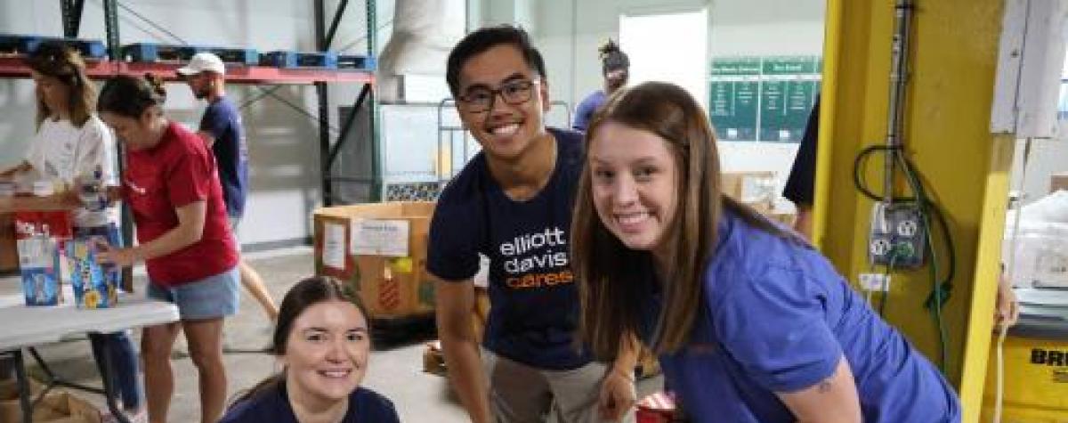 Three volunteers from Elliott Davis pose for the camera while sorting canned food items