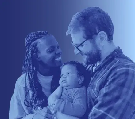 A mother and father holding their child, smiling at the baby.