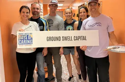 Ground Swell Capital volunteering for a painting project at 2025 Days of Caring. They are posing holding a sign with their name with painting tools