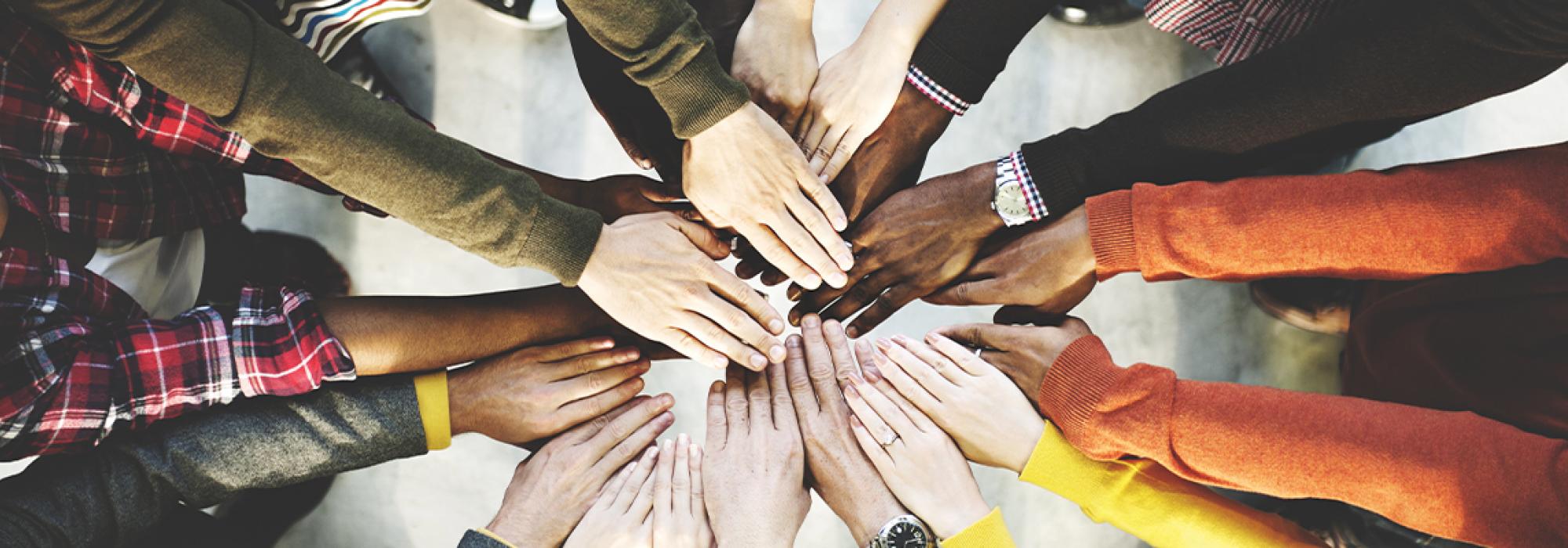 Photo of a dozen diverse people putting their hands into the middle of a circle
