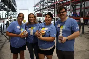 Four individuals wearing Tanger Outlet shirts hold school supplies for the school supply drive