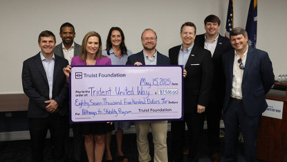 A group of 7 Truist Foundation members stand next to DJ Hampton, President and CEO of TUW. They are all standing behind a large check written to TUW from Truist for $87,500. The check is for the Pathways to Stability Program.