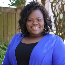 Candace has short dark hair with loose curls, she is wearing a royal blue blazer and black top. she is smiling looking at the camera