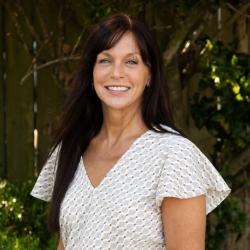 Photo of Elizabeth, she has long brown hair and is wearing a white patterned shirt.