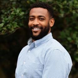 Photo of Samuel Bias. He has short dark hair and is wearing a blue and white checkered shirt, smiling at the camera
