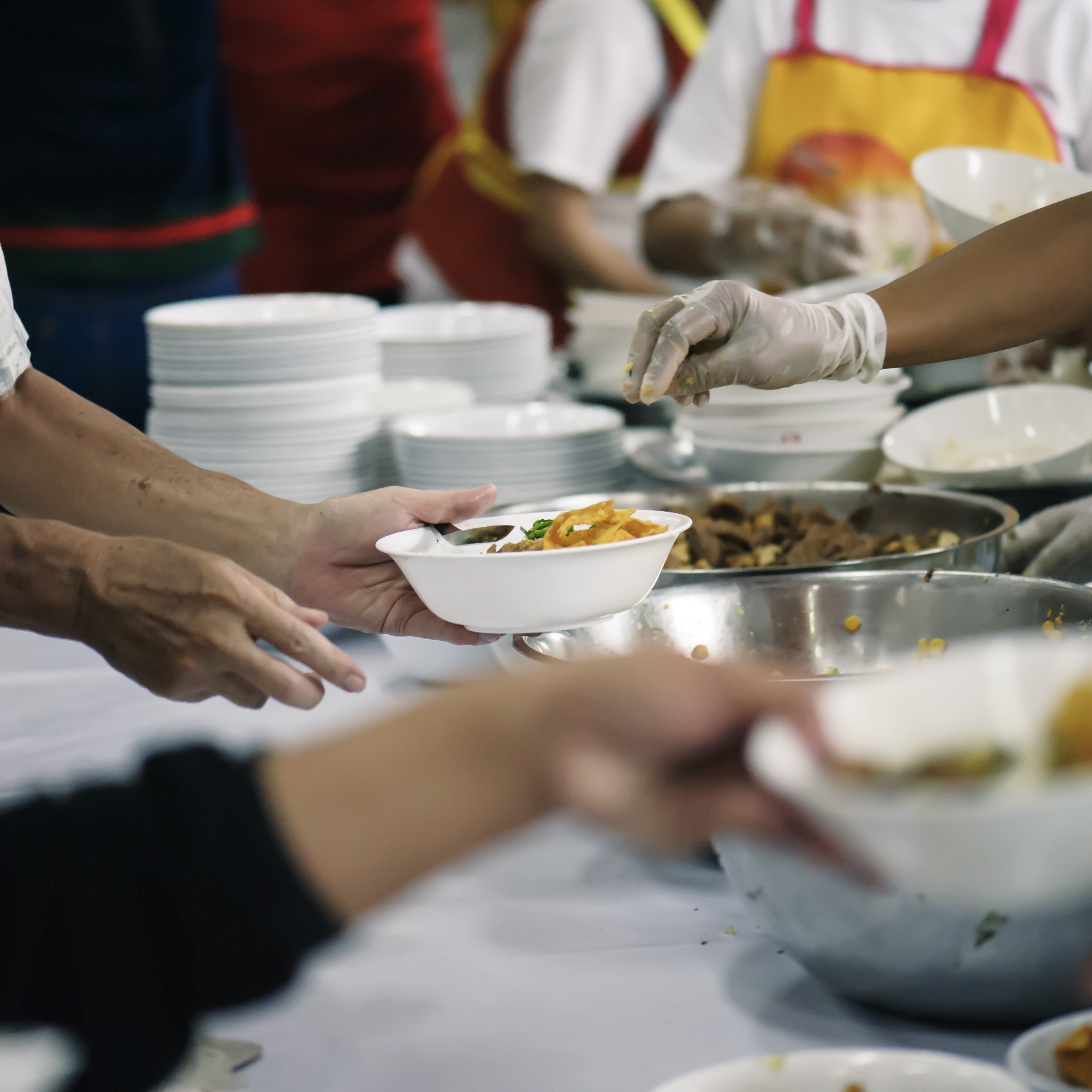 Hands are seen giving and taking bowls of food over a table.\