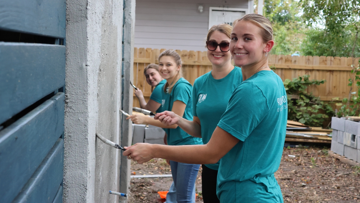 Four women painting a house and smiling at the camera
