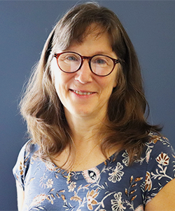Brenda is in a floral top and she is standing in front of a blue background. She is smiling in her headshot.