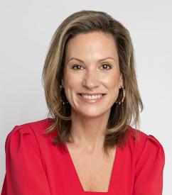 Melanie Stith is wearing a red top and has shoulder length blonde hair, she is smiling at the camera.