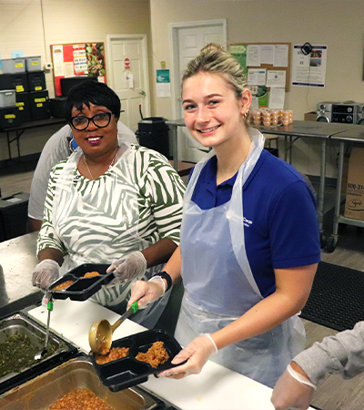 Two women smiling while preparing meals at the food bank
