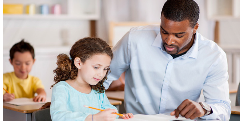 Teacher kneeling down next to a student writing in a notebook