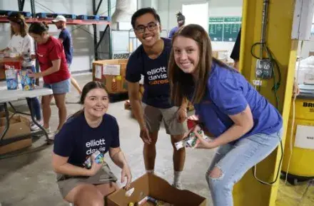 Three volunteers from Elliott Davis pose for the camera while sorting canned food items