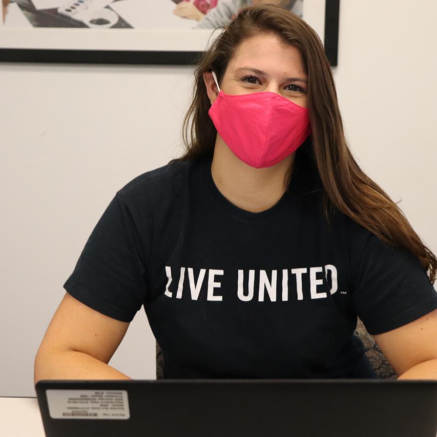 Woman wearing Live United shirt sitting at laptop.