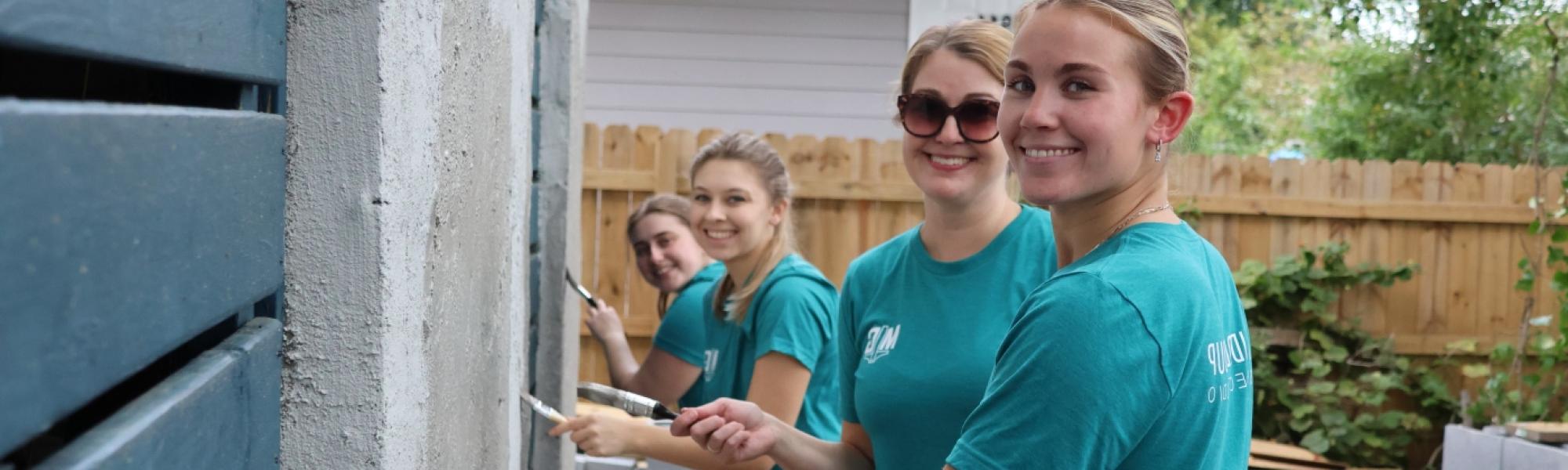 Four women painting a house and smiling at the camera